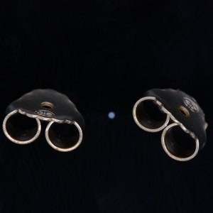 May include: Two gold-toned earring backs with a double-prong design. The backs are designed to hold a stud earring in place.