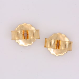 May include: A pair of gold-toned earring backs. The backs are round with a small opening in the center. They are designed to be used with post earrings.