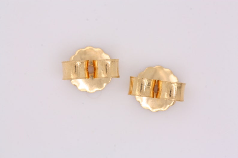 May include: A pair of gold-toned earring backs. The backs are round with a small opening in the center. They are designed to be used with post earrings.