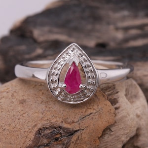 Op de afbeelding: Een zilveren ring met een peervormige robijn, gezet in een decoratieve zilveren setting.