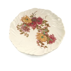 May include: A white ceramic plate with a scalloped edge features a floral design of pink, yellow, and green chrysanthemums.