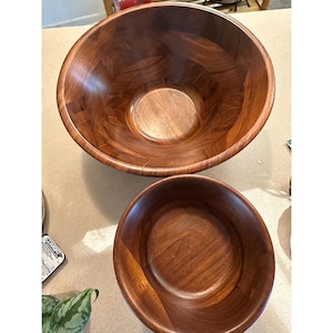 Könnte beinhalten: Zwei Holzsalatschüsseln. Die größere Schüssel befindet sich oben und die kleinere Schüssel unten. Beide Schüsseln bestehen aus dunkelbraunem Holz mit einem natürlichen Maserungsmuster. Die Schüsseln sind leer und scheinen neu zu sein.