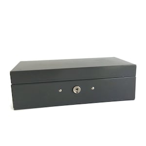 May include: A dark gray metal box with a keyhole and two small silver rivets on the front. The box is closed.
