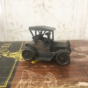 Könnte beinhalten: Ein vintage-artiger Bleistiftspitzer aus schwarzem Metall in Form eines Autos. Das Auto hat ein schwarzes Metalldach und ein detailliertes Design.