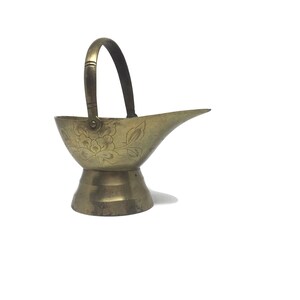 May include: A small, gold-coloured brass jug with a floral design and a handle. The jug has a round base and a spout.