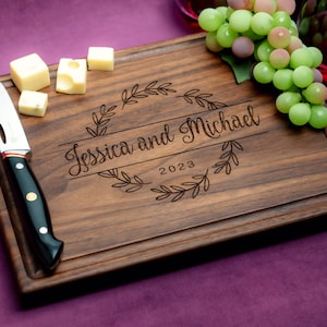 Handmade from natural hardwood personalized cutting board. Never stained, 100% food safe, only finished with food grade mineral oil and beeswax. 12x9 inches Walnut Wooden board with central design number 215 with first names and year.