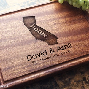 Handmade from natural hardwood personalized cutting board. Never stained, 100% food safe, only finished with food grade mineral oil and beeswax. 12x9 inches Mahogany Wooden board with central design number 602 with US state, first names, and date.