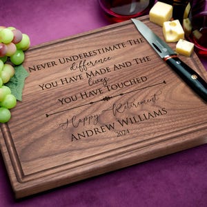Personalized walnut cutting board with happy retirement design displayed on purple background with grapes and cheese. Great gift for retired family members or coworkers.