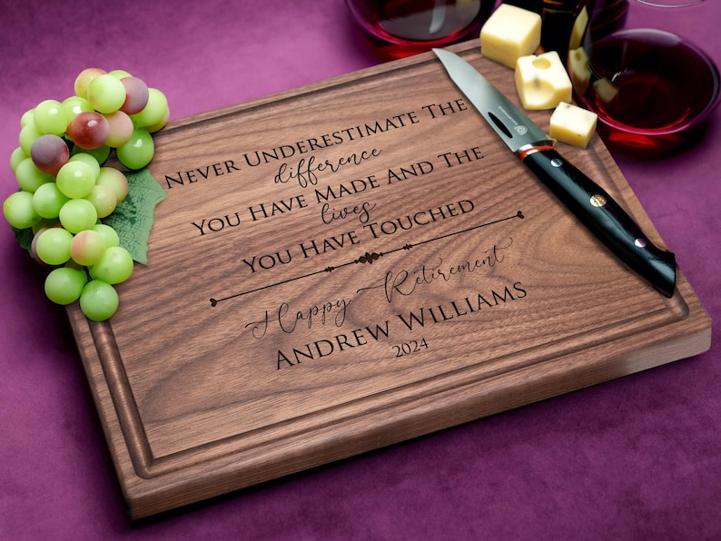 Personalized walnut cutting board with happy retirement design displayed on purple background with grapes and cheese. Great gift for retired family members or coworkers.