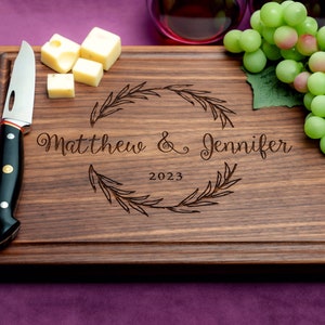 Handmade from natural hardwood personalized cutting board. Never stained, 100% food safe, only finished with food grade mineral oil and beeswax. 12x9 inches Walnut Wooden board with central wreath design number 413 with first names and date.