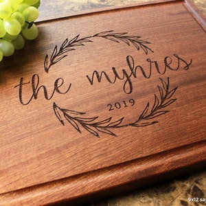 Handmade from natural hardwood personalized cutting board. Never stained, 100% food safe, only finished with food grade mineral oil and beeswax. 12x9 inches Mahogany Wooden board with central wreath design number 413 with first names and date.