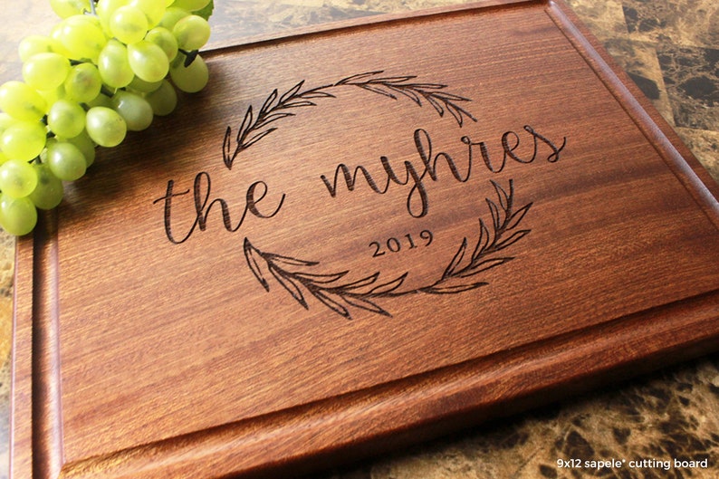 Handmade from natural hardwood personalized cutting board. Never stained, 100% food safe, only finished with food grade mineral oil and beeswax. 12x9 inches Mahogany Wooden board with central wreath design number 413 with first names and date.