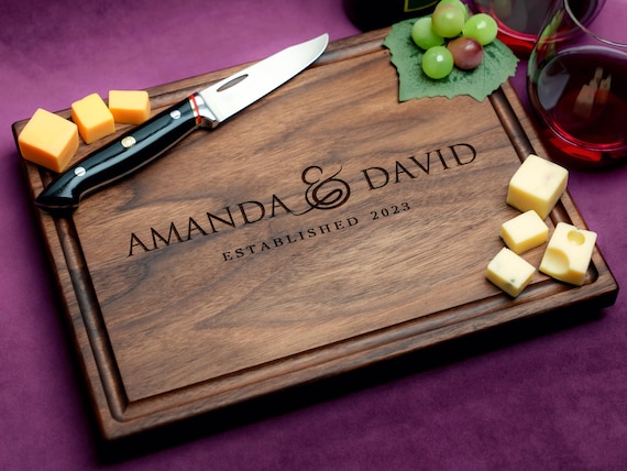 Walnut cutting board laser-engraved with a stylized ampersand — a genuinely clever couples symbol that doubles as wall art.