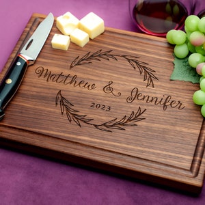 Handmade from natural hardwood personalized cutting board. Never stained, 100% food safe, only finished with food grade mineral oil and beeswax. 12x9 inches Walnut Wooden board with central wreath design number 413 with first names and date.