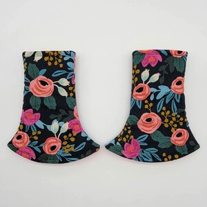 May include: Two fabric items with a floral pattern. The pattern features pink and coral roses, blue leaves, and yellow accents on a black background. The items have a flared bottom and a curved top.