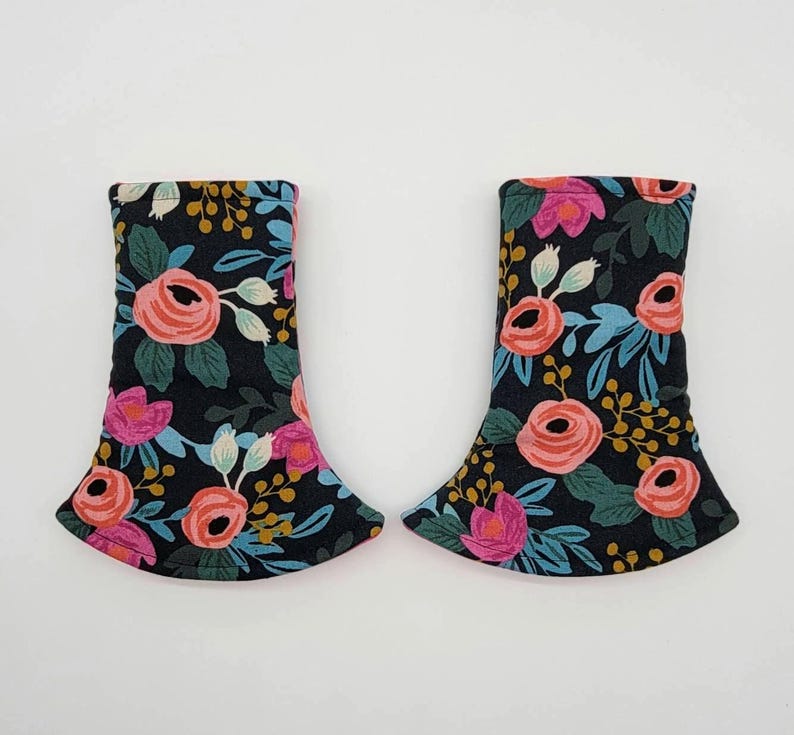 May include: Two fabric items with a floral pattern. The pattern features pink and coral roses, blue leaves, and yellow accents on a black background. The items have a flared bottom and a curved top.