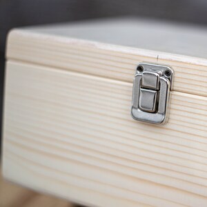 May include: A light wood box with a silver latch. The box has a natural wood grain and is made of solid wood.