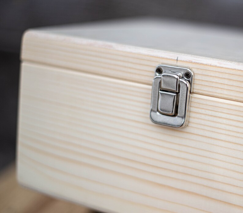 May include: A light wood box with a silver latch. The box has a natural wood grain and is made of solid wood.
