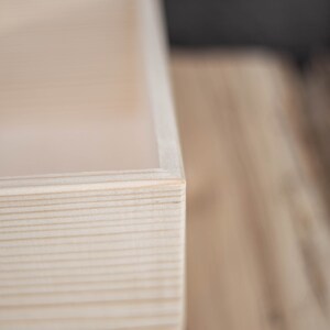 May include: Close-up of the corner of a natural wood box. The wood is light in colour and has a smooth, polished finish.