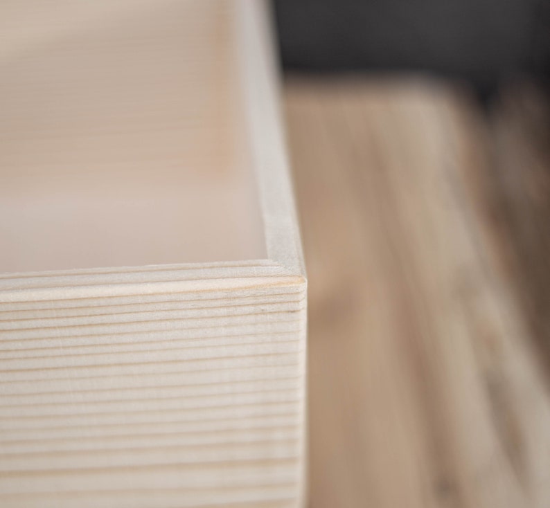 May include: Close-up of the corner of a natural wood box. The wood is light in colour and has a smooth, polished finish.