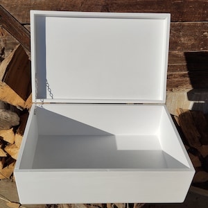 May include: White wooden box with a hinged lid and a metal chain attached to the inside of the lid. The box is open and empty.