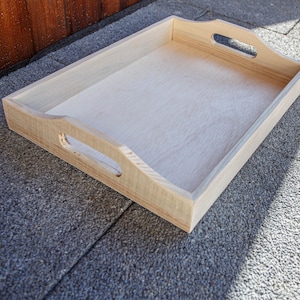 Può includere: Un vassoio da portata in legno naturale con due maniglie sui lati. Il vassoio è realizzato in legno chiaro e ha una superficie liscia.