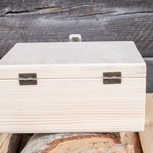 May include: A white wooden box with two brass hinges. The box is closed and sitting on a wooden surface.