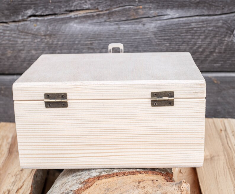 May include: A white wooden box with two brass hinges. The box is closed and sitting on a wooden surface.