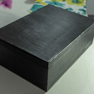 Könnte beinhalten: Eine schwarze Holzkiste mit einem Scharnierdeckel. Die Kiste ist aus dunklem Holz und hat eine glatte, polierte Oberfläche.