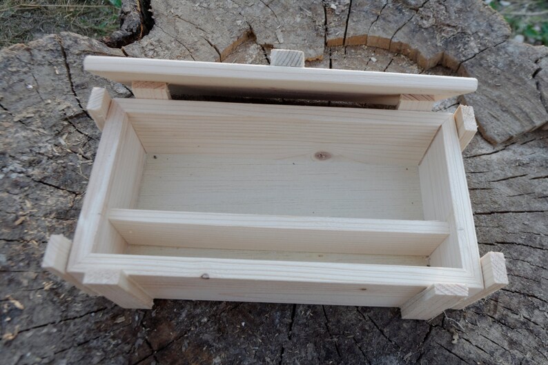 May include: A wooden box with a hinged lid and a divider inside. The box is made of light-colored wood and has a natural finish.