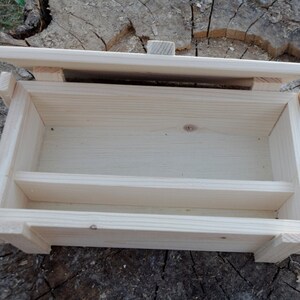 May include: A wooden box with a hinged lid and a divider inside. The box is made of light-colored wood and has a natural finish.