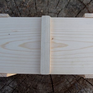 May include: A plain wooden box with a hinged lid and a wooden latch. The box is made of light-colored wood and has a smooth finish.