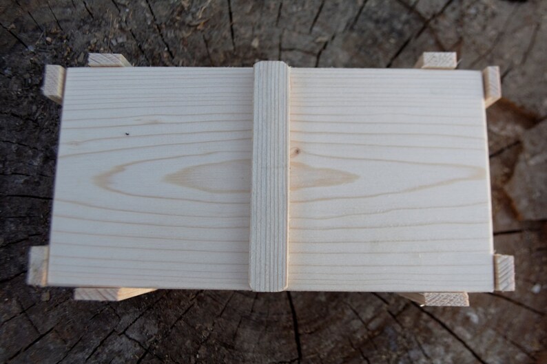 May include: A plain wooden box with a hinged lid and a wooden latch. The box is made of light-colored wood and has a smooth finish.