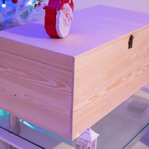 Pu&ograve; includere: Una scatola di legno naturale con un coperchio incernierato e una chiusura in metallo. La scatola &egrave; appoggiata su un tavolo di vetro con una base bianca.