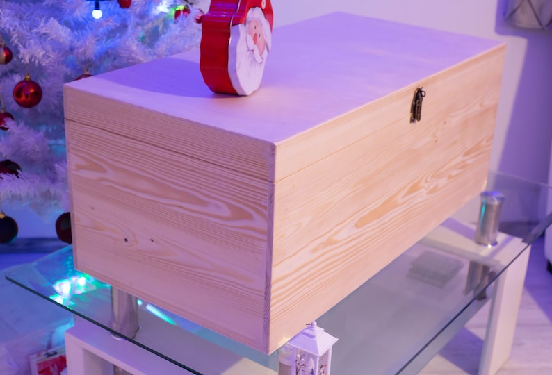 Pu&ograve; includere: Una scatola di legno naturale con un coperchio incernierato e una chiusura in metallo. La scatola &egrave; appoggiata su un tavolo di vetro con una base bianca.