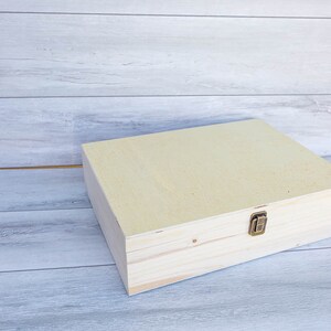 May include: A light wood box with a hinged lid and a brass latch. The box is closed and sitting on a light wood surface.