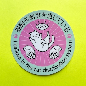 May include: A pink and green round sticker with a white cat, a stylized eye, and the text "猫配布制度を信じている" (which translates to "I believe in the cat distribution system") in Japanese.