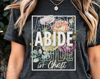 May include: A dark gray t-shirt with a floral design and the text "ABIDE in Christ" in white.