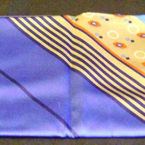 Peut inclure: Une écharpe en soie à motifs bleus et dorés avec un design de rayures diagonales. L'écharpe a un fond bleu clair avec des rayures dorées et un motif de petits cercles et ovales.