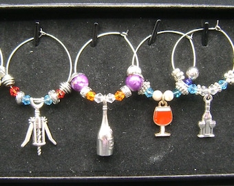 May include: Set of six wine glass charms with different charms, including a wine bottle, a corkscrew, a wine glass, and a bunch of grapes. Each charm is attached to a silver ring with colorful beads.