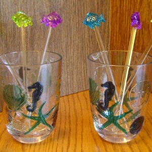 May include: Two clear glass tumblers with seahorse and starfish designs. Each glass has four colorful glass fish drink stirrers.