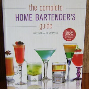 Puede incluir: La portada del libro The Complete Home Bartender's Guide con un fondo blanco y cócteles coloridos. El título del libro está en texto morado y el subtítulo en texto marrón. La portada del libro presenta una variedad de cócteles, incluyendo un martini verde, un cóctel rojo, un cóctel en capas y un cóctel en capas verde y naranja.