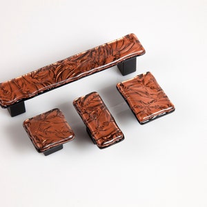 May include: Set of four copper glass cabinet knobs with a black metal base. The knobs feature a textured, swirling pattern.