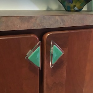 Pode incluir: Dois botões de armário triangulares com uma moldura de vidro transparente e um centro de vidro verde.