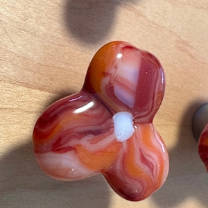 May include: A red, orange, and white agate flower-shaped cabinet knob. The knob has a swirl pattern and a white center.