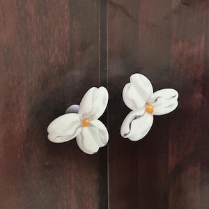 May include: Two white ceramic drawer pulls shaped like flowers with yellow centers. The pulls are mounted on a dark wood surface.