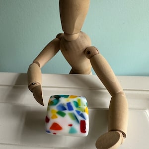 May include: A colourful, square-shaped glass cabinet knob with a white background and a mosaic of red, blue, green, and yellow pieces.