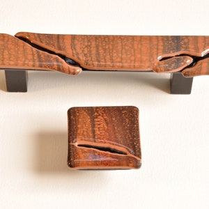 May include: A set of two brown and black glass cabinet knobs with a unique crackled finish. The larger knob is rectangular and the smaller knob is square.