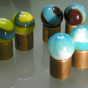 May include: Six glass marbles with different color patterns, each sitting on a brass stand. The marbles are blue, green, white, and brown.