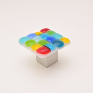 May include: Square cabinet knob with a white base and a colourful glass top. The glass top features a mosaic of small, round, coloured glass pieces in shades of blue, green, yellow, and red.